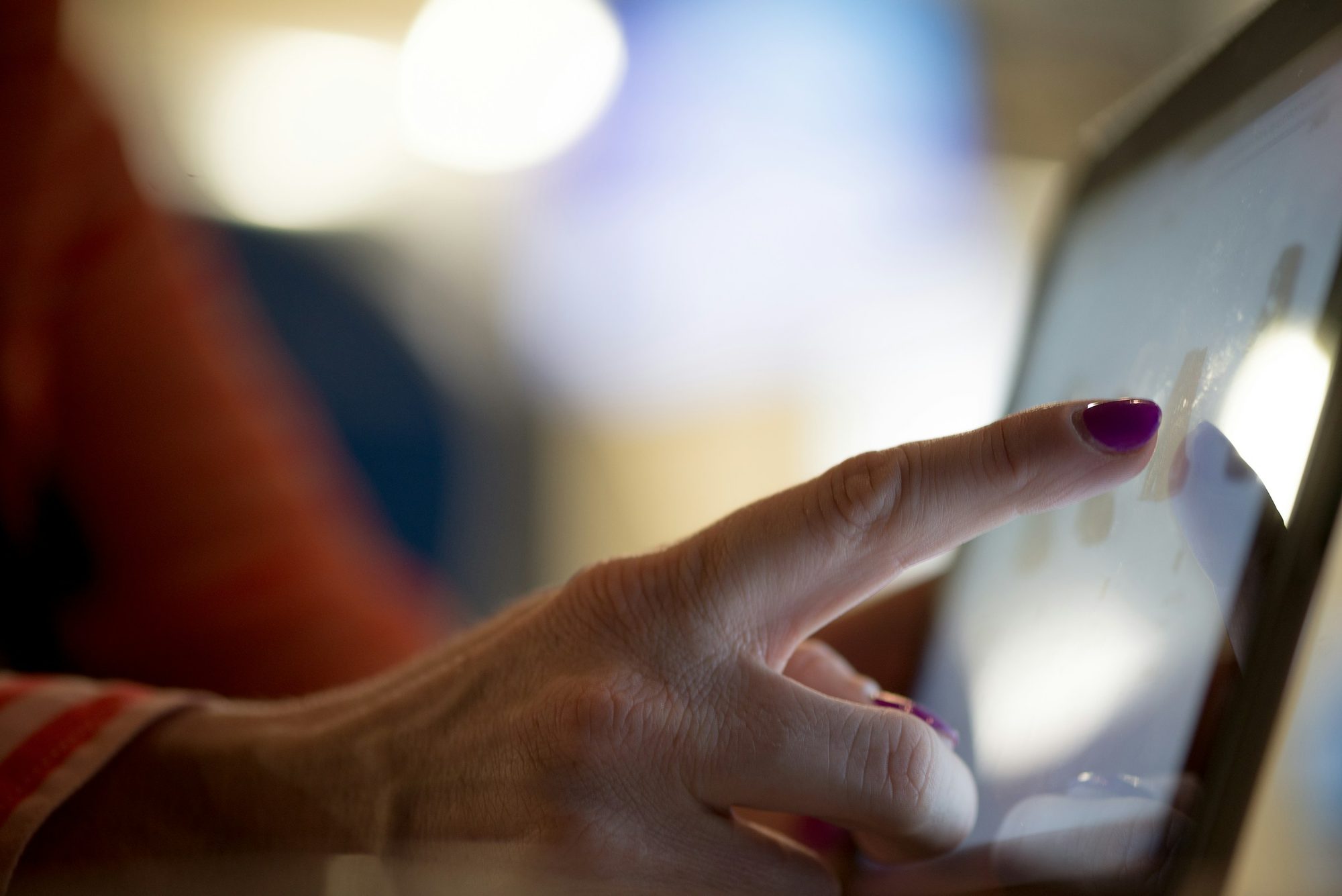 A hand touching a lit touchscreen in a restaurant